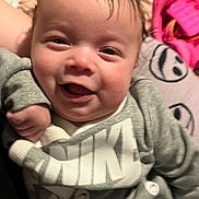 Kingston is registered to the contest to win money with this photo: baby, infant, child, smiling, portrait, face, eyes, mouth, cheeks, hand, clothing, sweatshirt, logo, nike, blanket, pillow, bed, indoor, close_up, happy