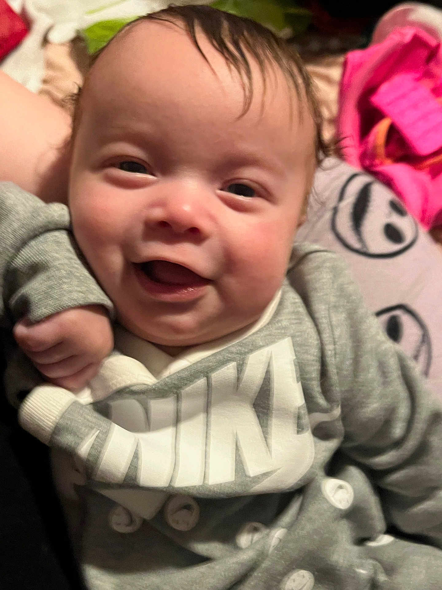 Kingston is registered to the contest to win money with this photo: baby, infant, child, smiling, portrait, face, eyes, mouth, cheeks, hand, clothing, sweatshirt, logo, nike, blanket, pillow, bed, indoor, close_up, happy