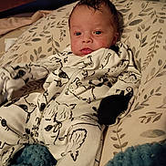 Kingston is registered to the contest to win money with this photo: baby, infant, onesie, animal_print, pillow, leaf_pattern, bed, blanket, sleepwear, face, head, expression, indoors, soft_lighting, cute, child, person, resting, cozy, young