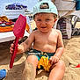 toddler, beach, sand, toy, shovel, cap, sunny, child, play, outdoor, barefoot, smiling, summer, vacation, sand_toys, plastic_toy, umbrella, chair, relaxation, holiday