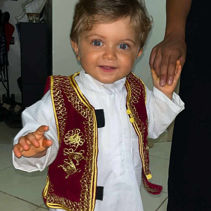 Lyam participe au concours pour gagner de l'argent avec cette photo : adult_hand, blue_eyes, child, cute, floor, footwear, happy, holding_hand, indoor, people, person, portrait, short_hair, smiling, tile_floor, toddler, traditional_clothing, vest, white_outfit, young_child