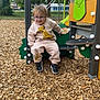 bench, child, daylight, glasses, green, happy, lion_king, nature, outdoor, person, play_equipment, playground, recreation, smiling, sneakers, sweatshirt, toddler, trees, wood_chips, yellow