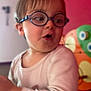 Noam participe au concours pour gagner de l'argent avec cette photo : blue_glasses, casual_clothing, child, closeup, colorful_background, curious_expression, expression, eyewear, face, glasses, indoor, light_shirt, person, playful, portrait, red_wall, short_hair, toddler, toy, young_child