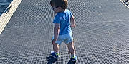 Noam participe au concours pour gagner de l'argent avec cette photo : blue_shirt, casual_clothing, child, daytime, dock, glasses, metal_surface, nature, outdoor, person, river, shadow, sky, summer, sunlight, toddler, trees, walking, water, white_shorts