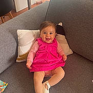 Avah participe au concours pour gagner de l'argent avec cette photo : baby, child, pink_dress, smiling, couch, pillow, indoor, clothing, footwear, happy, face, person, home, table, chair, laundry, curtain, phone_screenshot, text_overlay, living_room
