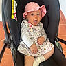 Avah a rejoint le concours — aidez-le/la à gagner de superbes lots ! baby, child, car_seat, pink_hat, dress, happy, smiling, indoor, footwear, socks, person, seat, cute, infant, expression, clothing, happy_face, young_child, floor, home