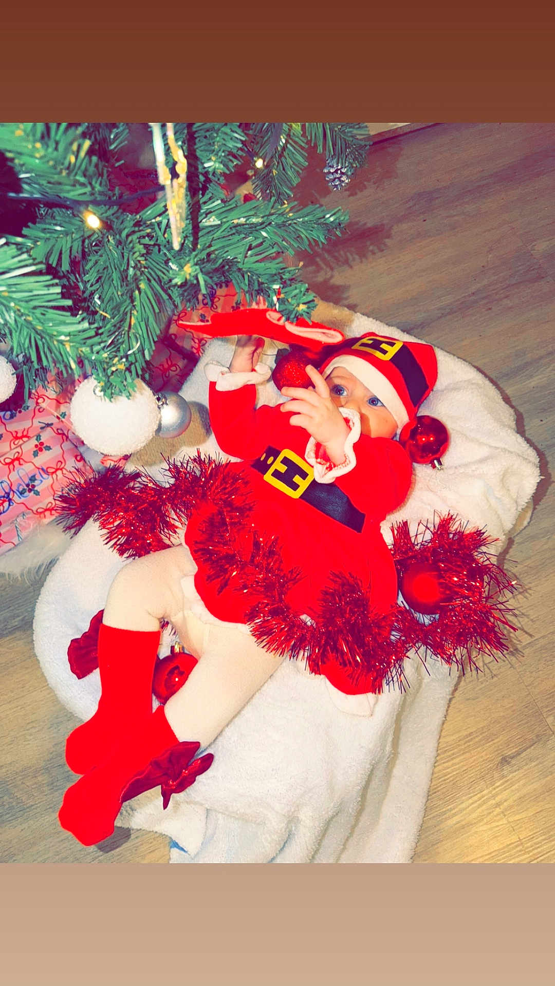 Shelsy a rejoint le concours — aidez-le/la à gagner de superbes lots ! baby, christmas_tree, red_clothing, santa_hat, ornaments, tinsel, blanket, floor, holiday, festive, infant, decorations, cute, child, indoors, celebration, seasonal, festivity, toy, cozy