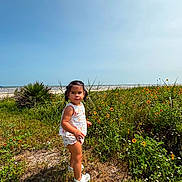 Vanessa is registered to the contest to win money with this photo: child, toddler, girl, portrait, outdoor, beach, ocean, seaside, wildflowers, flowers, meadow, grass, sunny, sky, waves, nature, summer, standing, clothing, shoes