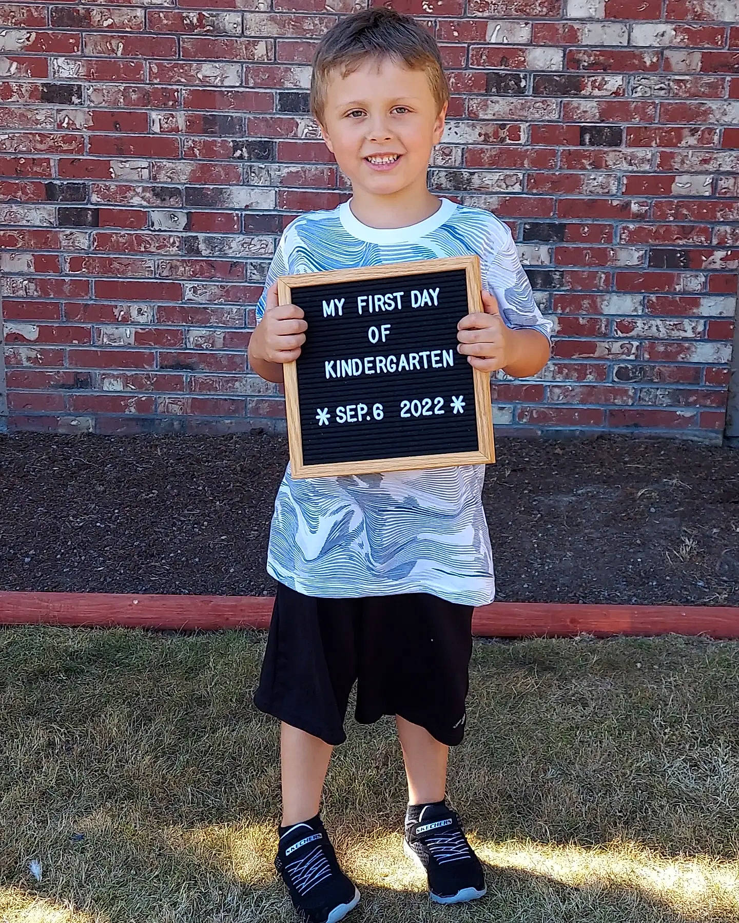 Kysen is registered to the contest to win money with this photo: brick, brickwork, child, clothing, denim, electric_blue, face, fun, grass, happy, joy, leisure, pattern, person, shorts, sleeve, smile, sportswear, t_shirt, toddler