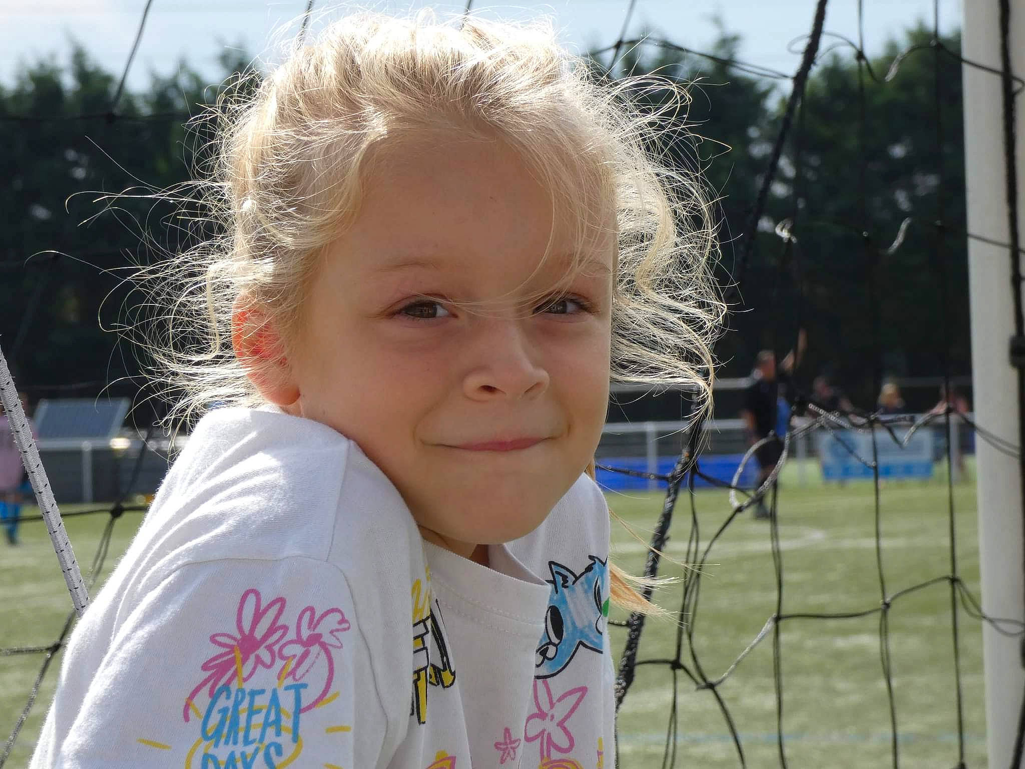 Lilou participe au concours pour gagner de l'argent avec cette photo : blond, child, chin, competition_event, fun, grass, happy, hoodie, iris, joy, leisure, net, outdoor_play_equipment, people_in_nature, person, player, portrait_photography, recreation, sky, smile