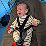 Gaspard a rejoint le concours — aidez-le/la à gagner de superbes lots ! baby, infant, smiling, laughing, bouncer_seat, five_point_harness, striped_onesie, soft_cushion, toy_wrist, colorful_toys, sock_toy, indoor, living_room, couch, pillow, happy, portrait, seated, playful, closeup