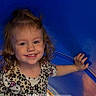 child, toddler, smiling, curly_hair, blue_tunnel, playground, patterned_shirt, happy, face, outdoor, play, person, cute, young_child, fun, daylight, joy, expression, clothing, leisure