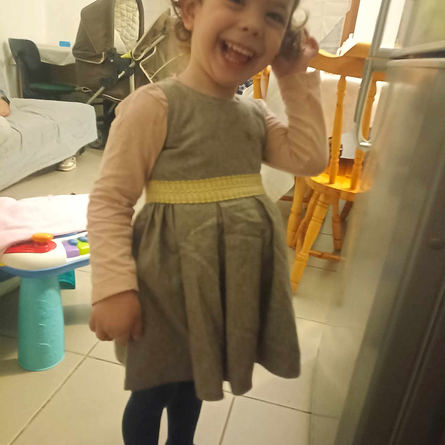 Mathilde Loureiro participe au concours pour gagner de l'argent avec cette photo : chair, child, clothing, curly_hair, dress, floor, furniture, happy, home, indoor, living_room, long_sleeve, person, smiling, socks, stroller, table, tile, toddler, toy