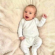 Tommy is registered to the contest to win money with this photo: baby, infant, smiling, white_onesie, fluffy_blanket, lying_down, happy, cute, child, person, portrait, cozy, soft_texture, indoors, newborn, skin, head, hand, footed_pajamas, sleepwear