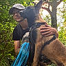 animal, camouflage, canine, crouching, dog, forest, greenery, hand, harness, hat, leaf, leash, man, nature, outdoor, path, pet, sunlight, tattoo, trees