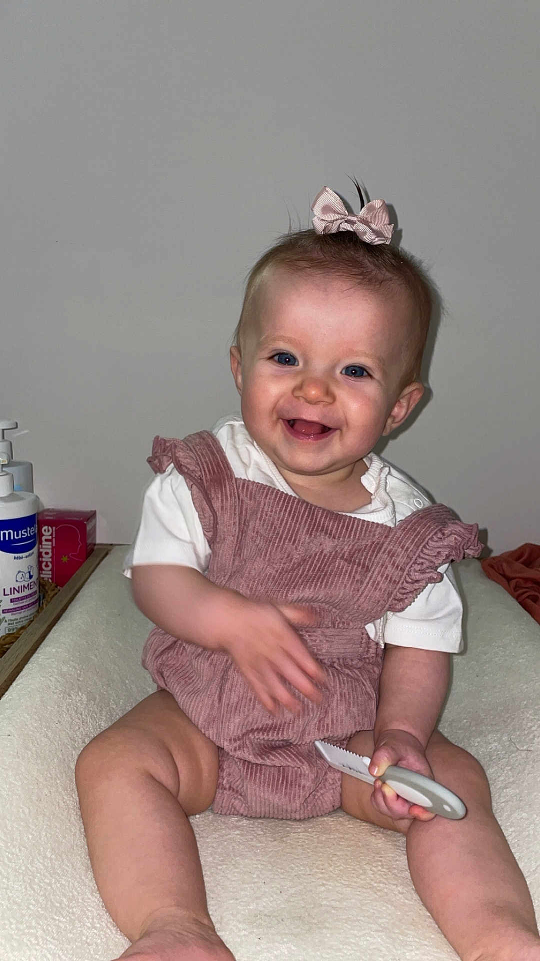 Elaïa a rejoint le concours — aidez-le/la à gagner de superbes lots ! baby, child, pink_bow, romper, smiling, blue_eyes, toy_knife, soft_surface, indoor, happy, sitting, cute, infant, baby_care, skin, hand, face, person, clothing, room