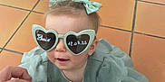 Elaïa a rejoint le concours — aidez-le/la à gagner de superbes lots ! toddler, child, baby, sunglasses, heart_shaped_glasses, dress, bow, hand, floor, tile, person, footwear, white_shoes, sock, indoor, cute, holding_hand, fashion, accessory, portrait