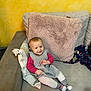 baby, casual, child, couch, cozy, cute, furniture, happy, home, indoor, knitted_dress, person, pillow, relaxed, seated, smiling, soft_texture, striped_socks, toddler, yellow_wall