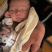 Klark Kent Thomas is registered to the contest to win money with this photo: baby, newborn, sleeping, blanket, hand, adult_hand, wristband, hospital_id, swaddle, closeup, portrait, face, eyelids, nose, cheek, soft_blanket, cozy, medical_tape, barcode, infant_clothing