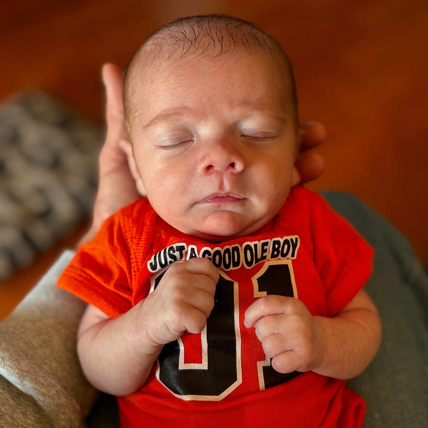 Klark Kent Thomas joined the competition — help win amazing prizes! baby, bokeh, casual_clothing, closeup, cute, face, hands, indoor, infant, newborn, onesie, orange_onesie, parent_hand, peaceful, portrait, sleeping, soft_skin, tiny_fingers, tshirt_print, wooden_floor