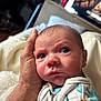baby, newborn, infant, face, eyes, hand, adult_hand, blanket, onesie, skin, portrait, close_up, bedding, cozy, indoor, living_room, television, background_blur, expression, sleepy