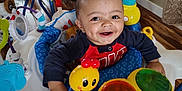 Jakai is registered to the contest to win money with this photo: baby, child, smiling, dimples, activity_center, toys, colorful, indoor, floor, table, chair, wood_floor, curtain, person, happy, infant, play, seat, face, young