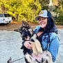 background_blur, cap, daylight, denim_jacket, dog, fur, german_shepherd, happy, holding, outdoor, person, pet, playful, puppy, sidewalk, smiling, tail, trees, vehicle, woman