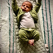 Legend joined the competition — help win amazing prizes! baby, infant, child, quilted_mat, green_clothing, white_shirt, striped_bedspread, barefoot, relaxed, lying_down, indoor, cute, small_feet, raised_arms, cozy, soft_texture, portrait, sleepwear, resting, young