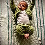 baby, infant, child, quilted_mat, green_clothing, white_shirt, striped_bedspread, barefoot, relaxed, lying_down, indoor, cute, small_feet, raised_arms, cozy, soft_texture, portrait, sleepwear, resting, young