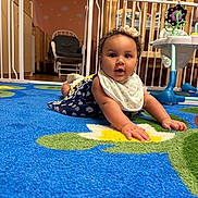 Zara joined the competition — help win amazing prizes! baby, baby_furniture, bib, blue, carpet, child, crib, curly_hair, cute, dress, floor, flower_pattern, headband, indoor, infant, looking, nursery, person, play_area, smiling