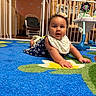 baby, baby_furniture, bib, blue, carpet, child, crib, curly_hair, cute, dress, floor, flower_pattern, headband, indoor, infant, looking, nursery, person, play_area, smiling