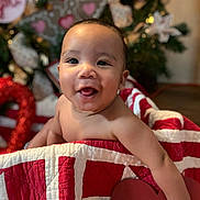 Micah is registered to the contest to win money with this photo: baby, child, smiling, quilt, red, white, heart, christmas_tree, holiday, decorations, gingerbread, indoors, portrait, cute, happy, face, person, festive, background, warm