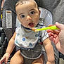 baby, high_chair, bib, baby_food, spoon, hand, feeding, indoor, child, cute, expression, person, seat, clothing, food, table, infant, mouth_open, looking, skin