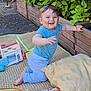 baby, child, smiling, outdoor, toy, mat, cushion, plant, greenery, wooden_planter, grass, happy, clothing, blue_shirt, pants, face, person, play, nature, daylight