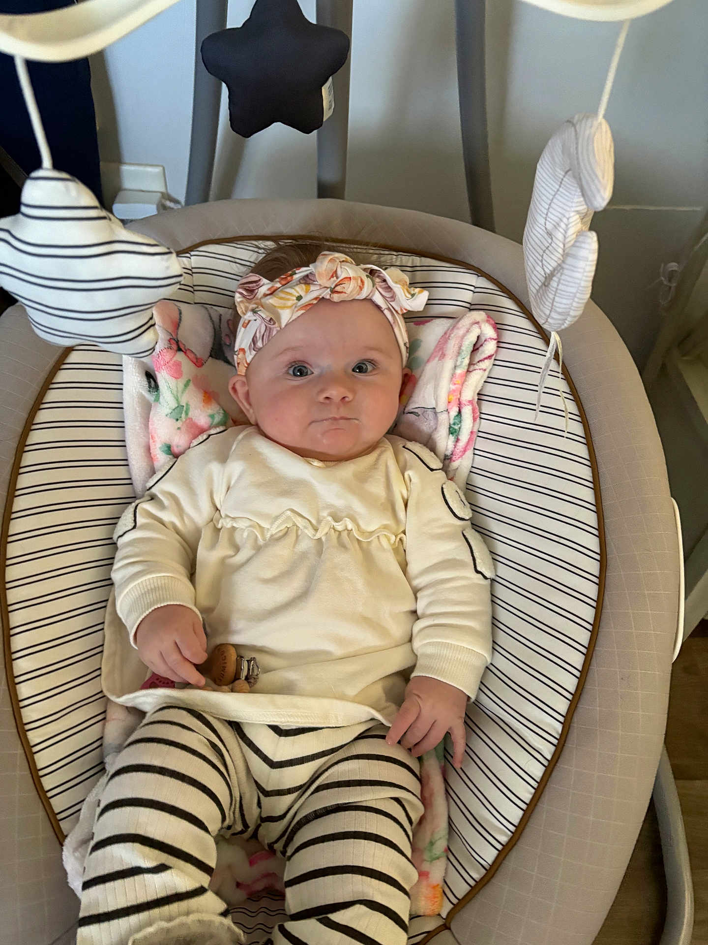 Olivia is registered to the contest to win money with this photo: baby, infant, headband, striped_clothing, baby_seat, toy, star_shaped_toy, cloud_shaped_toy, blanket, indoors, cute, child, person, striped_leggings, soft_toys, relaxing, portrait, wide_eyes, floral_pattern, hand