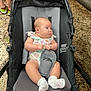 Oaklynn is registered to the contest to win money with this photo: baby, stroller, onesie, socks, blanket, infant, child, person, seated, curious, side_view, black_stroller, gray_cushion, pink_blanket, tattoo, leg, sneakers, stone_wall, outdoor, casual