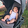 baby, stroller, outdoor, grass, white_onesie, tongue_out, happy, infant, seat, playful, sunlight, child, person, relaxing, summer, casual, expression, cute, baby_boy, wheeled_vehicle