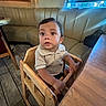 Brahim is registered to the contest to win money with this photo: toddler, child, high_chair, wooden_chair, table, restaurant, indoor, curious, seated, clothing, short_sleeve, brown_hair, face, eyes, mouth, booth_seating, window, purse, floor, tile_flooring