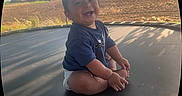 Brahim is registered to the contest to win money with this photo: baby, child, smiling, sitting, trampoline, outdoor, sunlight, nature, tree, grass, fence, farm, diaper, tshirt, happy, portrait, young_child, play, shadow, grassland