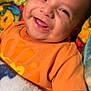 baby, smiling, orange_shirt, blanket, colorful, portrait, happy, infant, face, child, cute, lying_down, toddler, clothing, warm, cozy, indoors, skin, expression, young