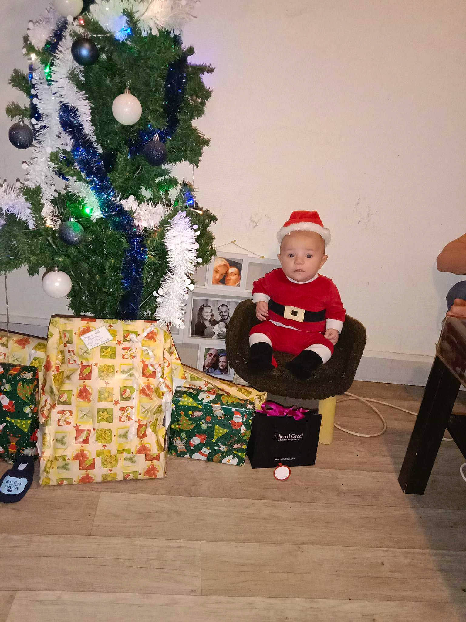 Maxence a rejoint le concours — aidez-le/la à gagner de superbes lots ! blurred, christmas, christmas_decoration, christmas_eve, christmas_ornament, christmas_tree, event, flooring, fun, holiday, holiday_ornament, joy, lap, ornament, person, plant, room, sitting, smile, toddler