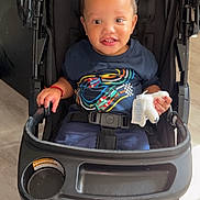 Kazire is registered to the contest to win money with this photo: toddler, child, stroller, sneakers, smile, indoor, clothing, hair, hand, seatbelt, footwear, floor, black, blue, toy, baby, person, cute, happy, portrait