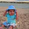 Lian is registered to the contest to win money with this photo: barefoot, beach, blue_clothing, child, clouds, lake, outdoors, patterned_clothing, portrait, sand, shoreline, sitting, sky, smiling, summer, sun_hat, sunset, text_overlay, toddler, water