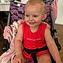 toddler, child, smile, red_dress, stroller, blanket, indoor, happy, blue_eyes, baby, seatbelt, person, cute, skin, hand, face, hair, clothing, pink, black