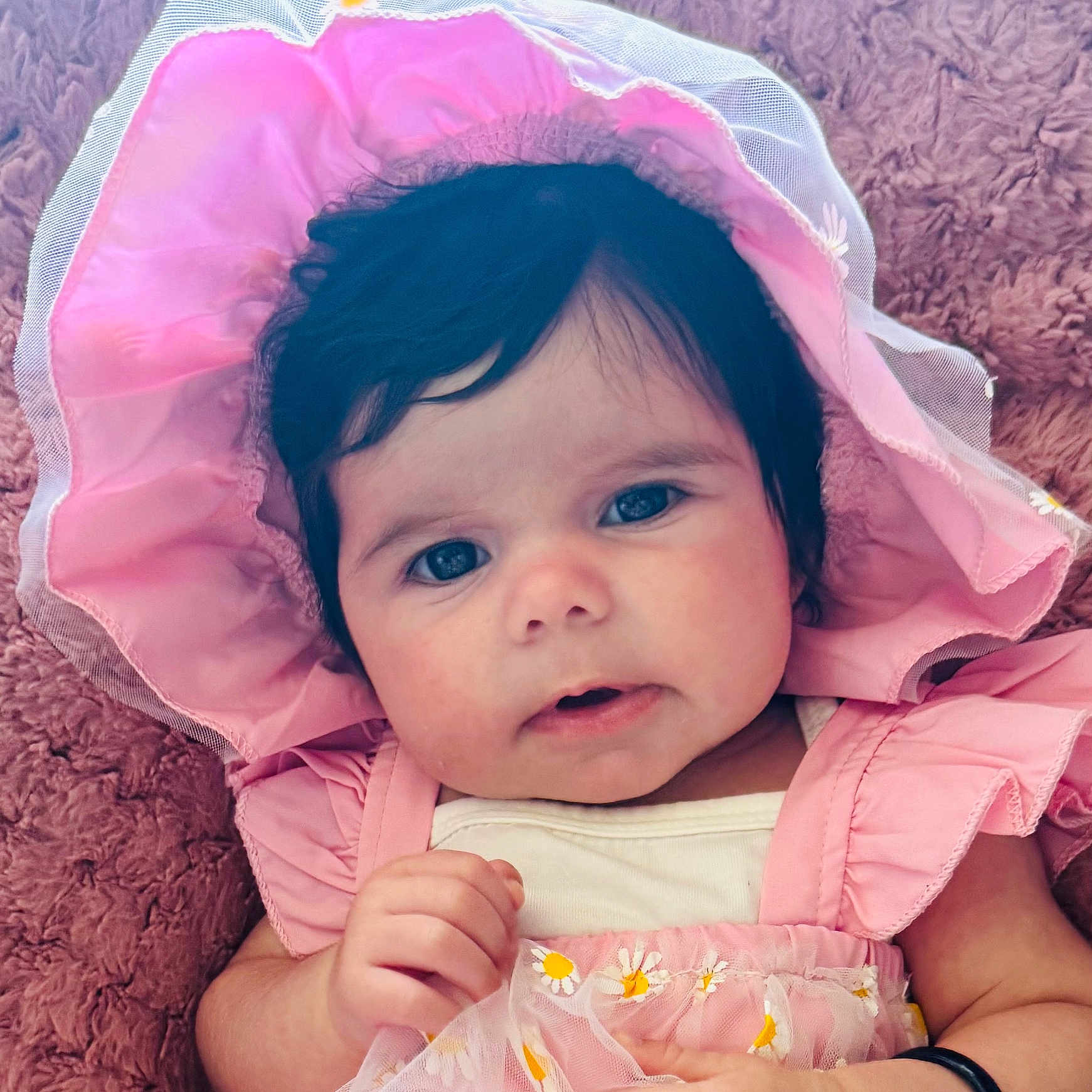 Kohinoor is registered to the contest to win money with this photo: adorable, baby, baby_fashion, child, closeup, clothing, cute, dark_hair, eyes, face, flower_pattern, hand, infant, lying_down, pink_bonnet, pink_dress, portrait, skin, soft_blanket, toddler