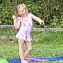 child, swimsuit, water_sprinkler, backyard, grass, fence, summer, play, outdoor, greenery, spray, fun, person, nature, water, young, girl, daylight, casual, motion