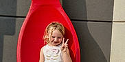 Lunah is registered to the contest to win money with this photo: child, girl, dress, red_spoon, sculpture, peace_sign, smile, outdoor, sunlight, shadow, rocks, concrete_wall, happy, blonde_hair, casual_shoes, playful, posing, young, cute, colorful