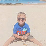 Nino participe au concours pour gagner de l'argent avec cette photo : beach, blue_shirt, boats, boy, casual, child, happy, nature, outdoor, play, rocks, sand, shorts, smile, stick, summer, sunglasses, sunny, vacation, water