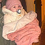 baby, pacifier, blanket, knitted_hat, adult, green_hoodie, cozy, wrapped, warm_clothing, indoor, portrait, child, person, face, holding, soft_texture, pink_blanket, curious_eyes, night, warm_lighting