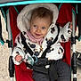 baby, child, stroller, jacket, pacifier, smile, hood, clothing, seatbelt, red, black, white, knit_pants, outdoor, infant, happy, cute, person, sitting, playful